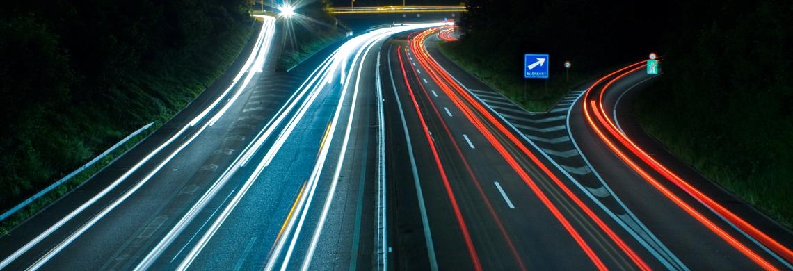 Man sieht eine Autobahn bei Nacht und das verschwommene Licht der Scheinwerfer.